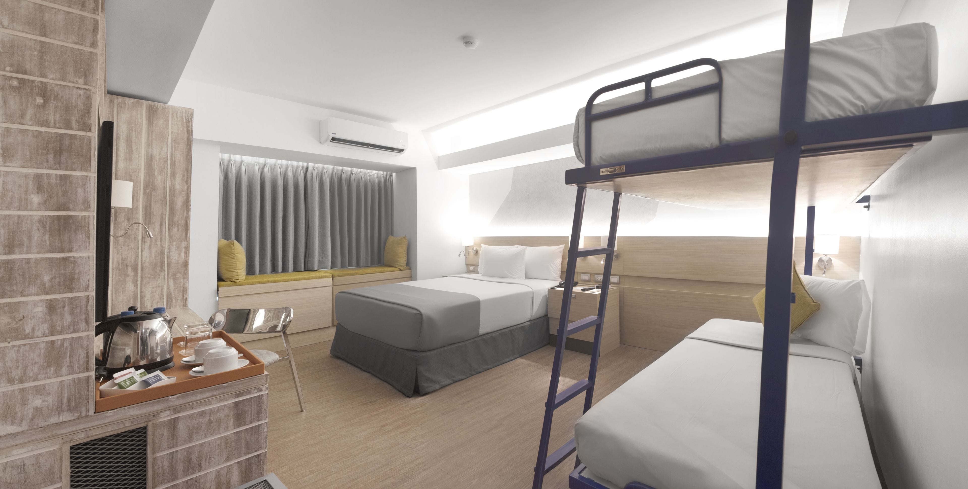 Una habitación de hotel moderna con literas, un escritorio con hervidor y una ventana con cortinas.