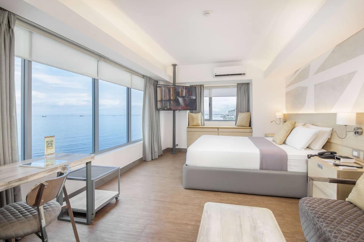 Een moderne hotelkamer met een groot raam, een bed, een bureau en een stoel.