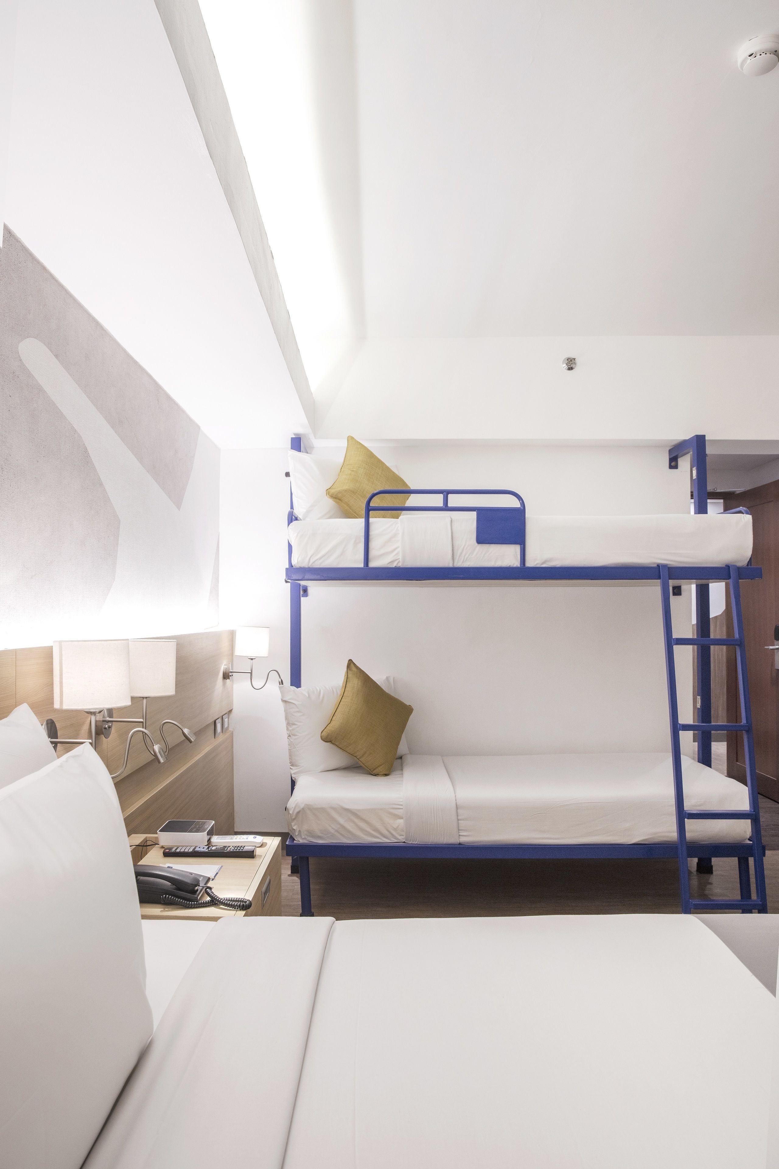 A bunk bed room with a wooden desk, a lamp, and a phone.