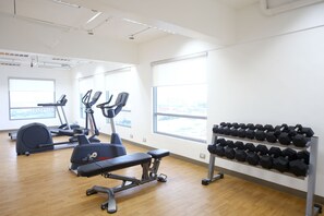 A gym with cardio machines, a bench, and a rack of dumbbells.