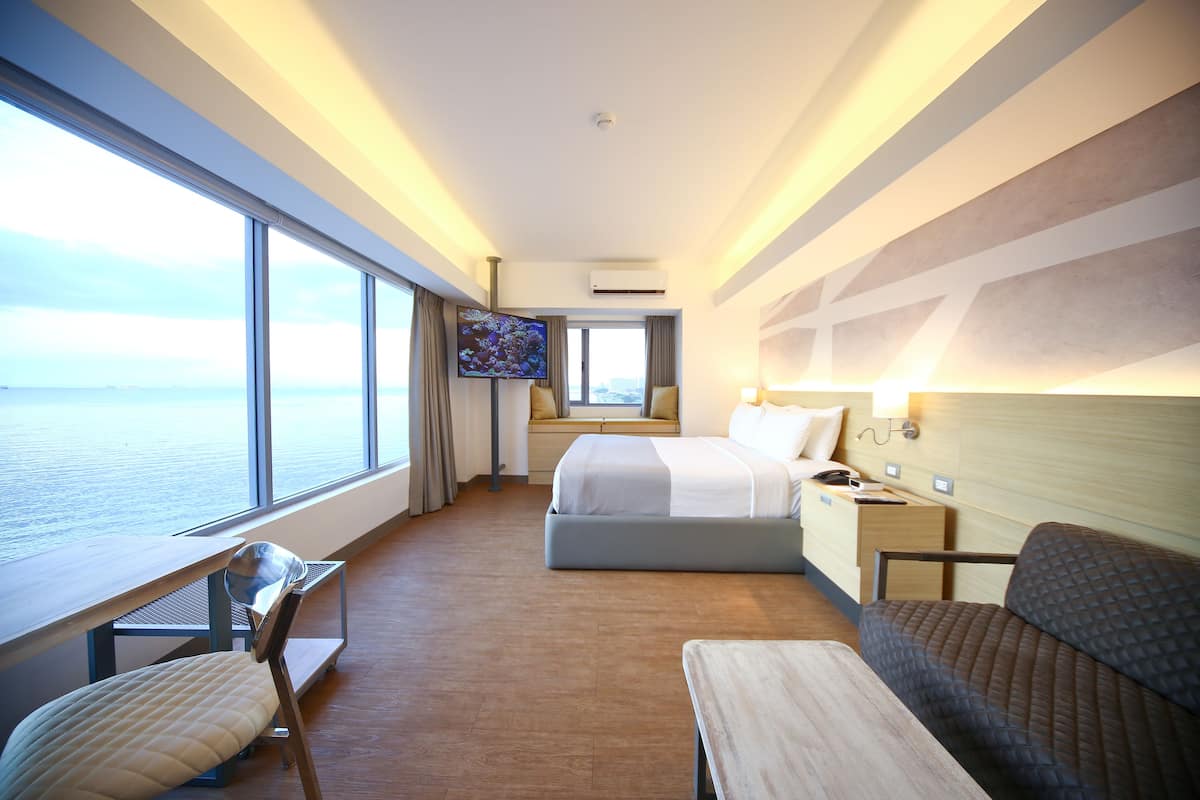 Een hotelkamer met een groot raam, een bed, een bureau, een stoel en een televisie.
