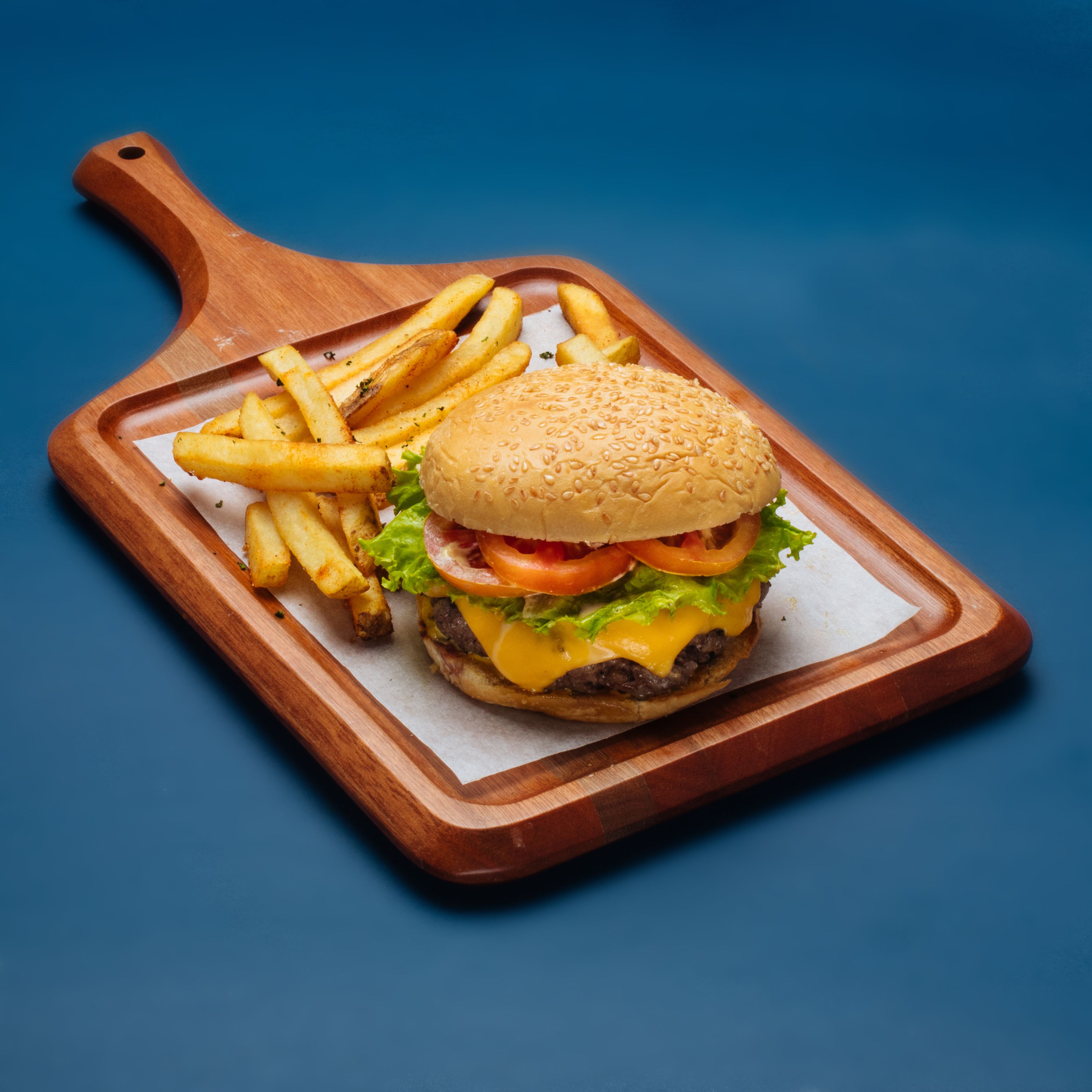 A burger with fries on a wooden board.