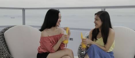 Dos personas sentadas en sillas de mimbre con vista al mar.