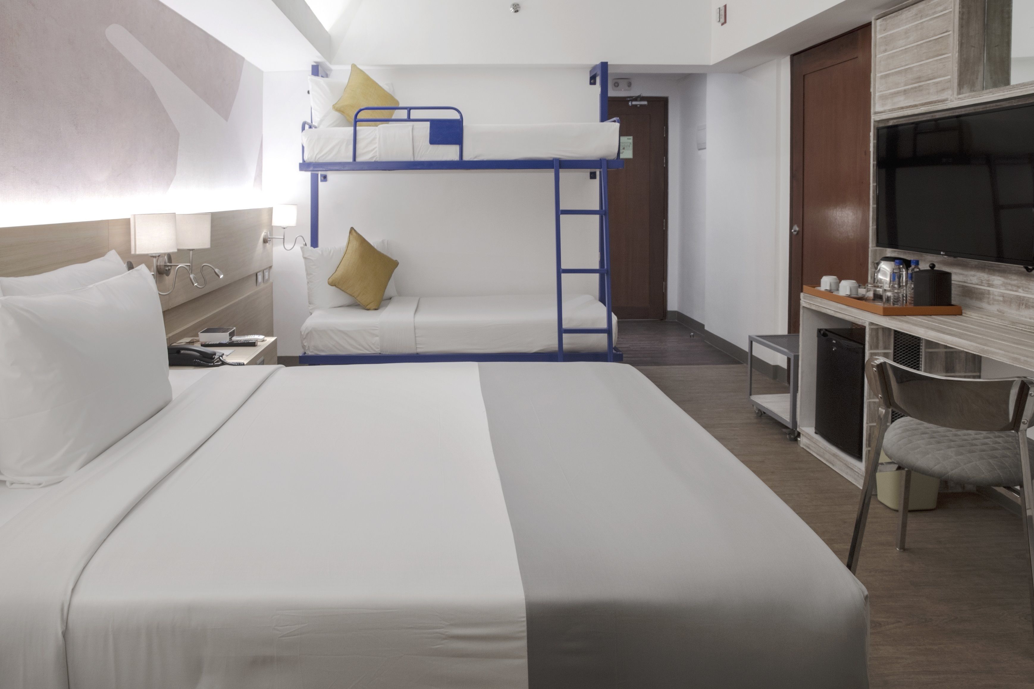 A hotel room with a bunk bed, a desk with a chair, a TV, and a small kitchenette.