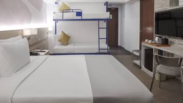 Habitación de hotel con literas, un escritorio con silla, televisión y una kitchenette pequeña.