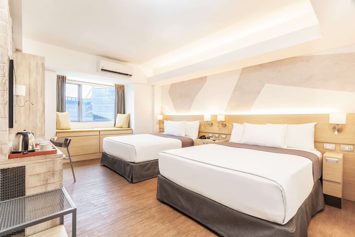 Een hotelkamer met twee bedden, een bureau, een stoel, een raam met gordijnen en een luchtverkoeler aan de muur.