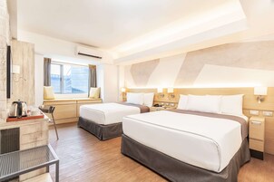 Ett hotellrum med två sängar, ett skrivbord, en stol, ett fönster med gardiner och en väggmonterad luftkonditioneringsanläggning.