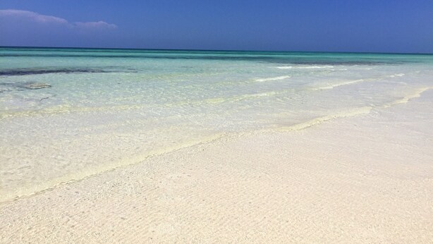 Une plage à l’eau turquoise et au sable blanc.