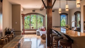 Eine geräumige Küche mit einem langen Holztisch, Barhocker und einem großen Fenster mit Blick ins Freie.