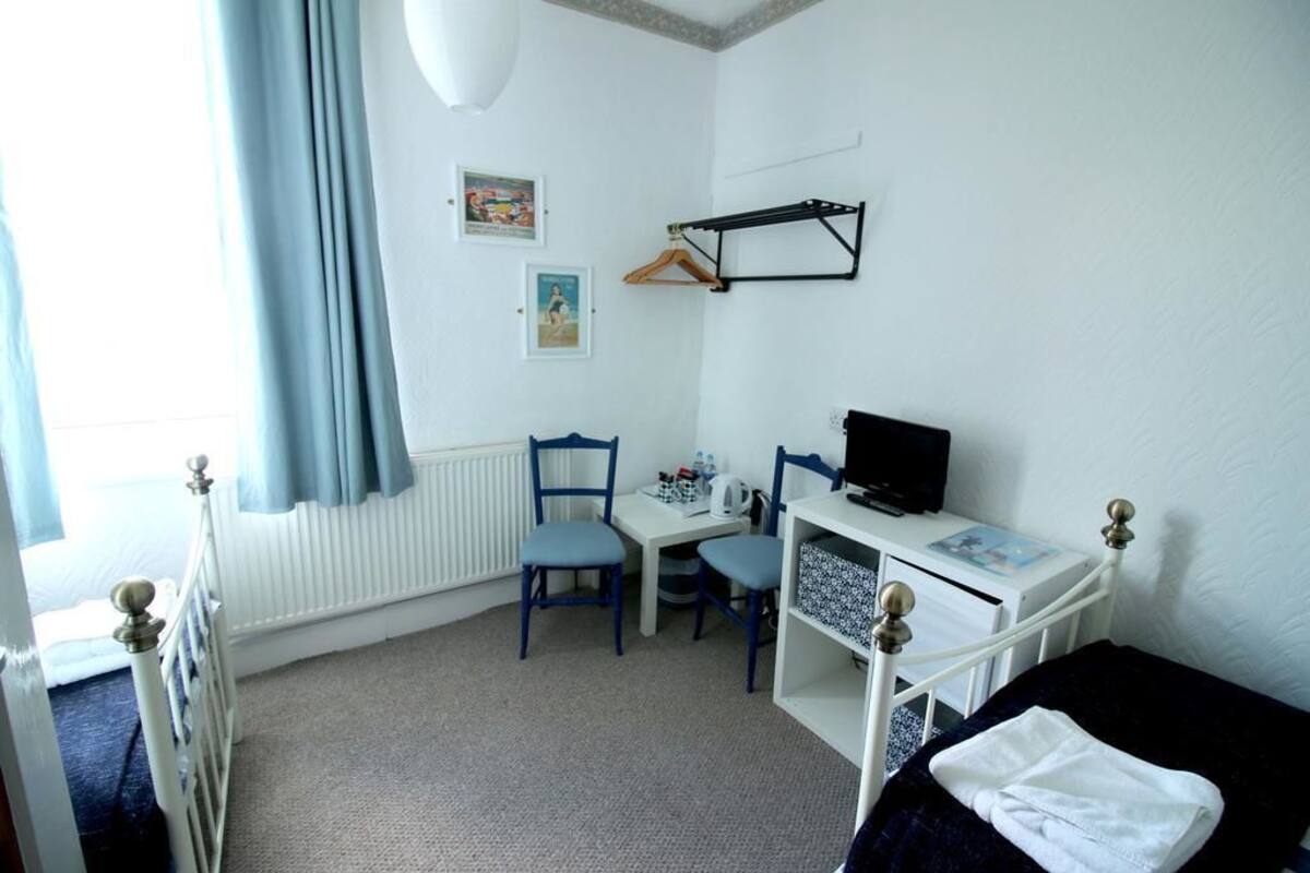 A child's bedroom with a white bed, a desk with a computer, two chairs, and a radiator.