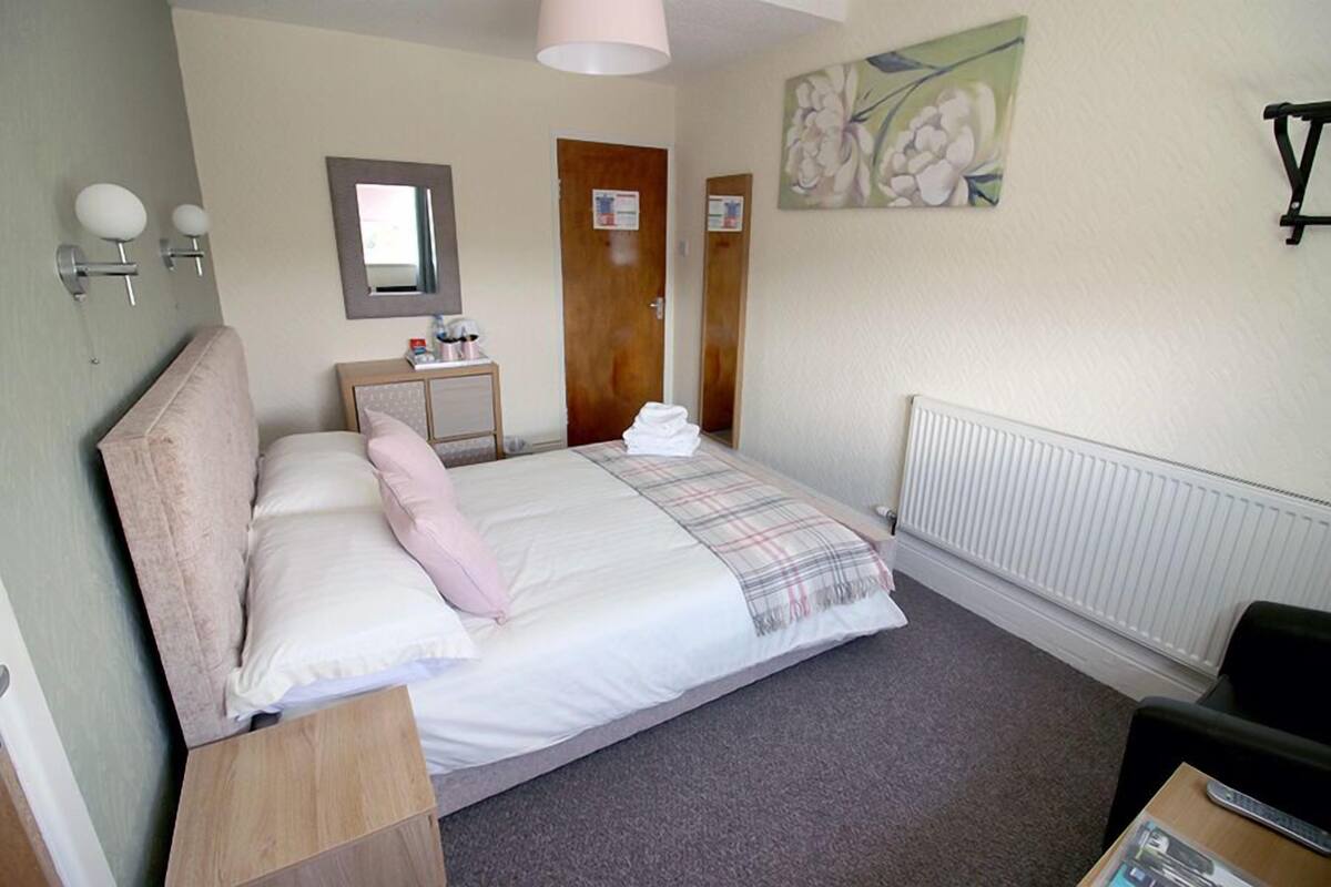 A bedroom with a bed, bedside table, mirror, and a painting on the wall.