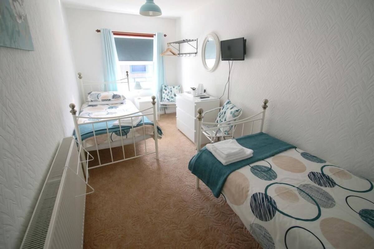 A bedroom with two single beds, a dresser, a chair, a desk, a mirror, and a television.