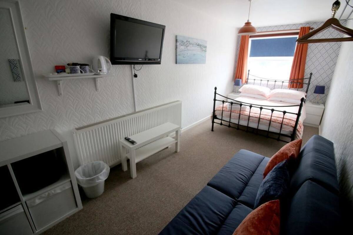 A bedroom with a bed, a TV, a radiator, a bench, and a sofa.