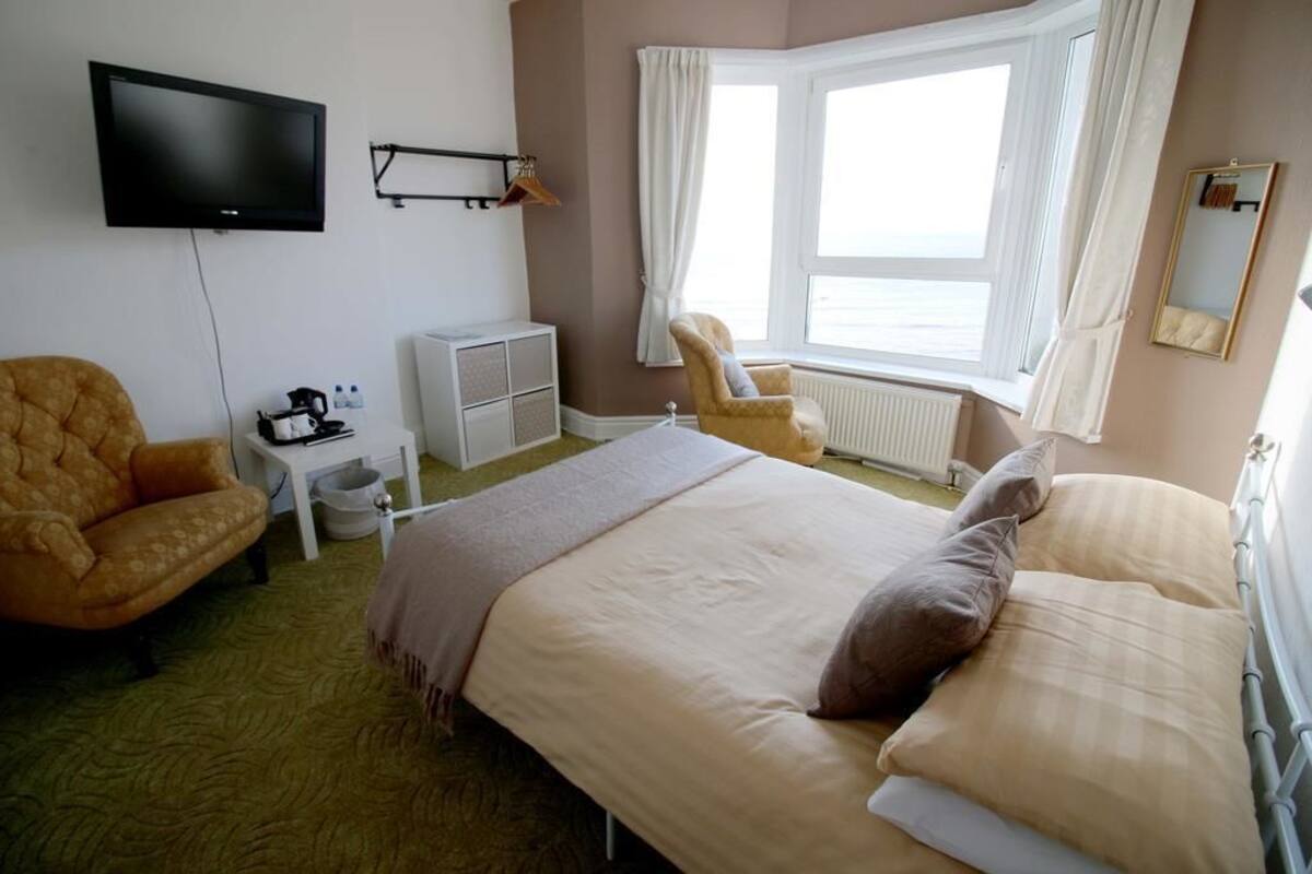 A hotel room with a bed, a chair, a television, a small table, and a window with curtains.