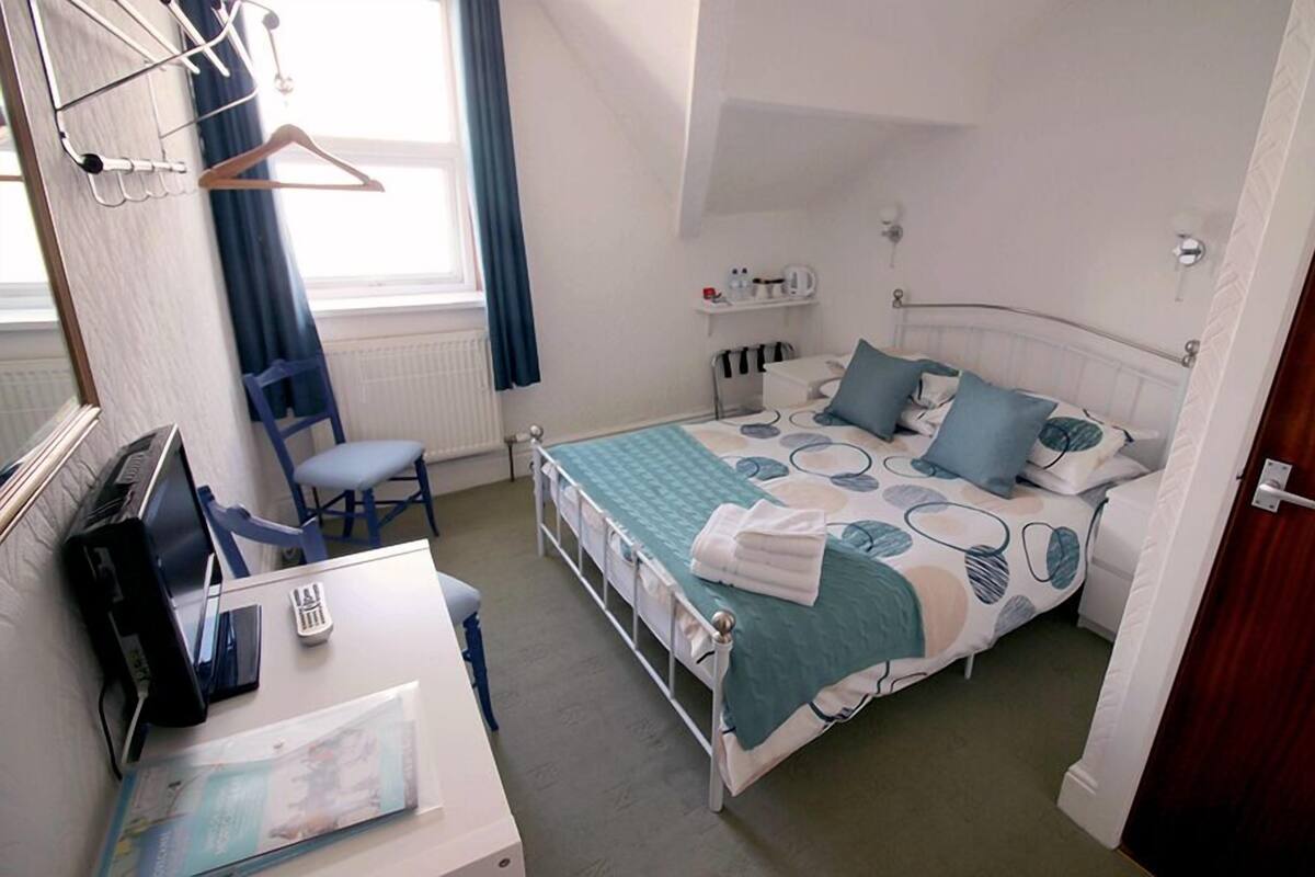 A bedroom with a bed, a desk, a chair, a radiator, and a window with curtains.
