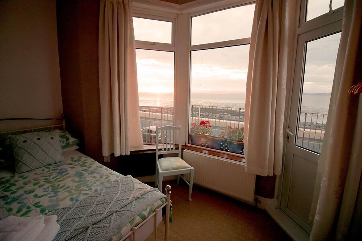 A bedroom with a bed, a chair, and a window with a view of the sea.