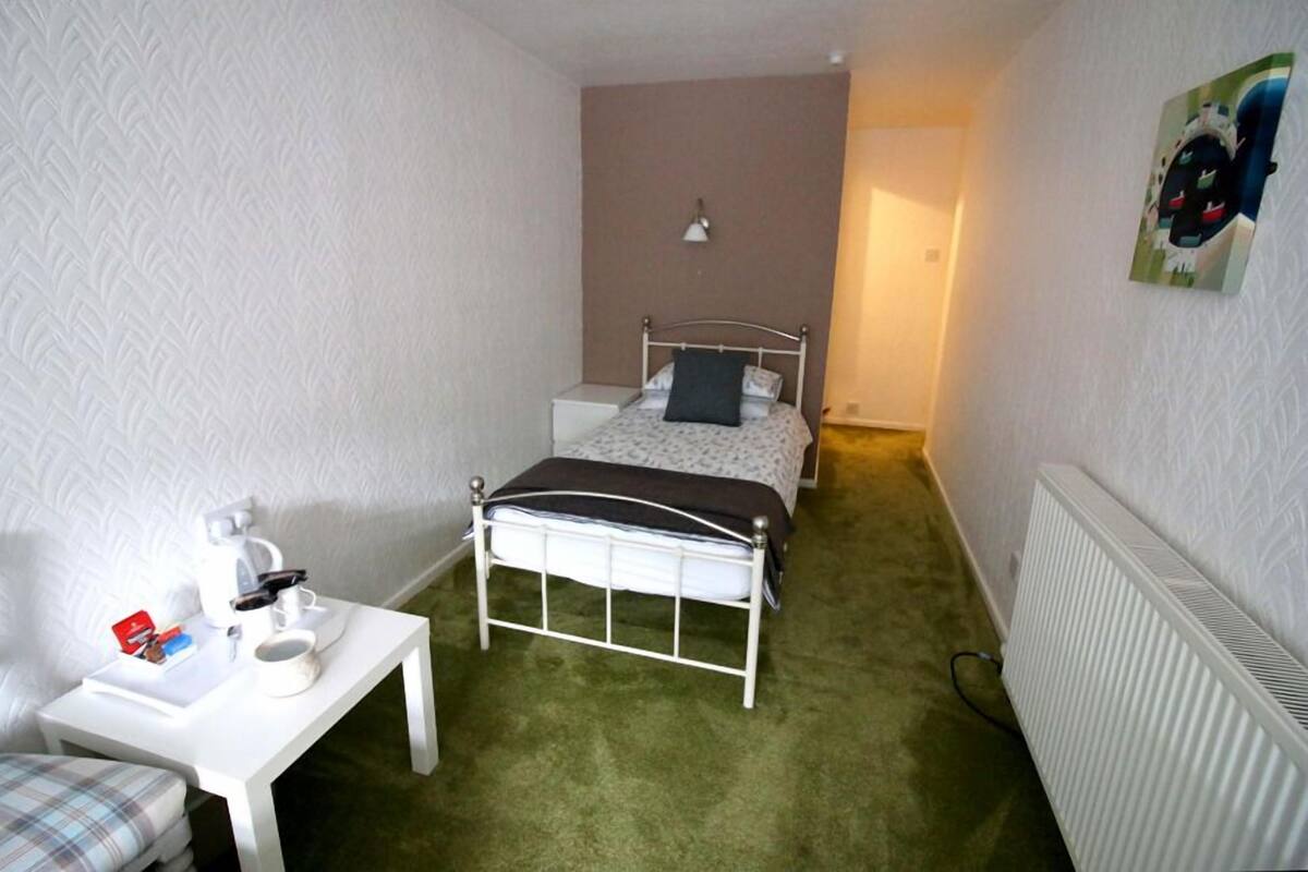 A small, narrow hotel room with a single bed, bedside table, and a radiator.
