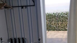 Quarto de hotel com cama, pequena escrivaninha, janela com vista para o mar e varanda com grade de metal.