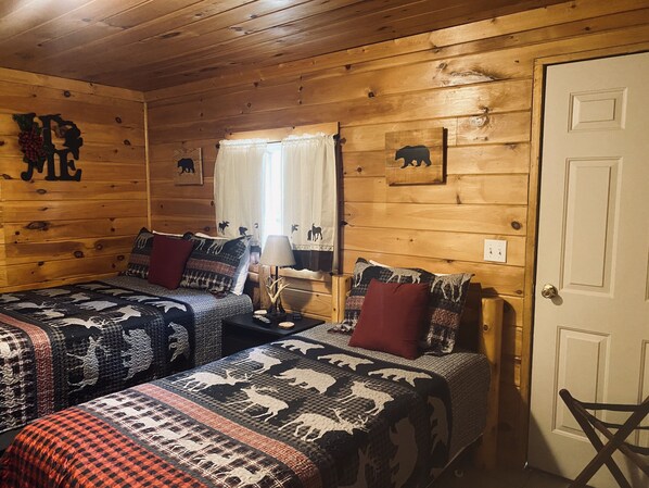 A cabin with two beds, a wooden ceiling, a window with curtains, and a door.