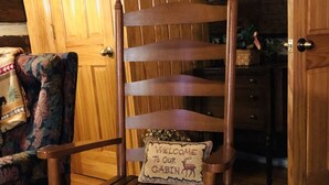 Un fauteuil à bascule en bois, agrémenté d’une pancarte indiquant « Bienvenue dans notre chalet », un tapis à motifs et des murs en bois.