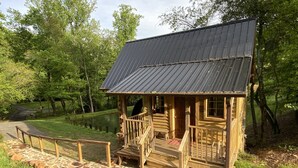 Une cabane en bois avec un toit en métal, un chemin de pierres et une zone herbeuse avec des arbres.