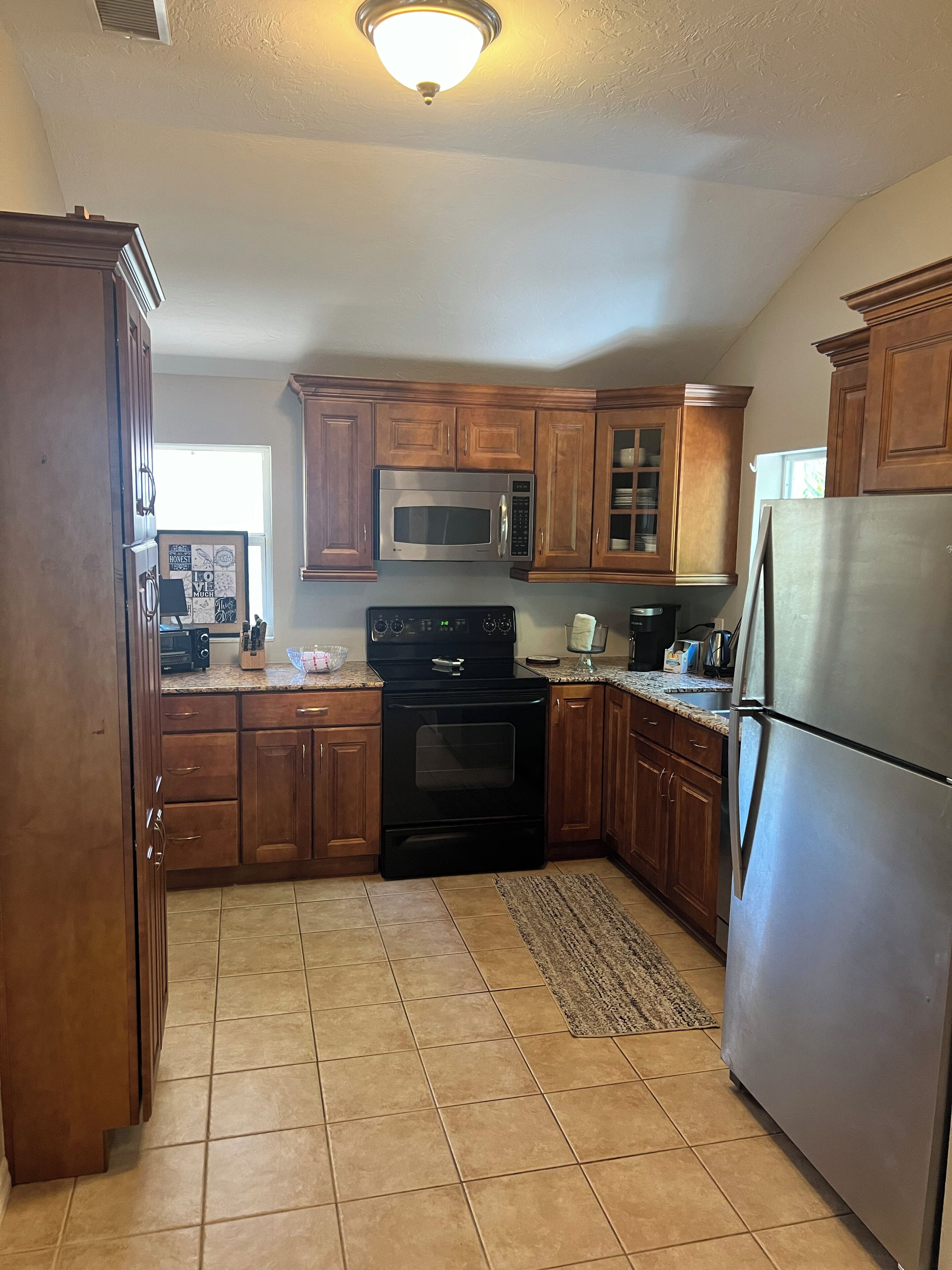A kitchen with wooden cabinets, a stainless steel refrigerator, a microwave, and a stove.