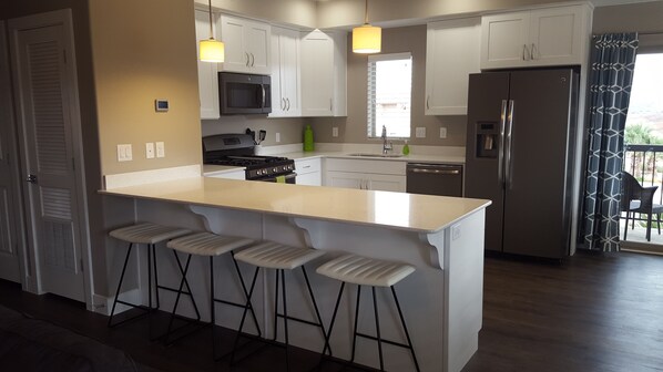 A modern kitchen with white cabinetry, a large island with bar stools, stainless steel appliances, and pendant lighting. - Estancia Resort! New beauty in St George with heated pool and pickleball (Saint George)