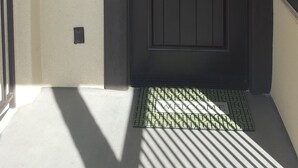 Une porte de couleur sombre, dotée d’un clavier pour l’ouverture, d’une alarme incendie et d’un paillasson à l’entrée.