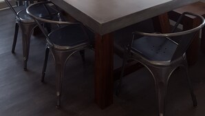 Un coin repas comprenant une table rectangulaire, six chaises, un saladier en verre transparent contenant des pommes vertes et un luminaire suspendu.