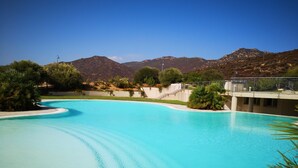 Una piscina de diseño curvo, rodeada de vegetación y con montañas al fondo.