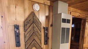 Una stanza con pannelli di legno, un tavolo e due sedie, una sveglia e una bocchetta di ventilazione.
