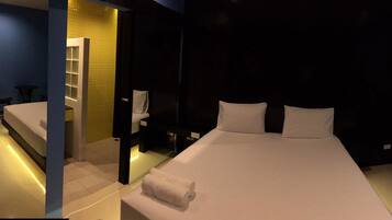 Habitación de hotel con una cama grande, una mesita de noche, un taburete pequeño, un espejo y un baño con inodoro y lavabo.