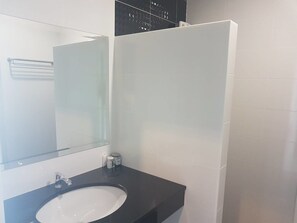 A bathroom with a white sink, a mirror, and a black countertop. - The Bed Hotel (Phitsanulok)