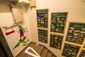 Un espace d’accueil avec un panneau indiquant la direction à prendre vers la gauche, un escalier et un mur orné de photographies encadrées représentant la Malaisie, Singapour, le Sarawak, Mulu, le Vietnam et les Philippines.