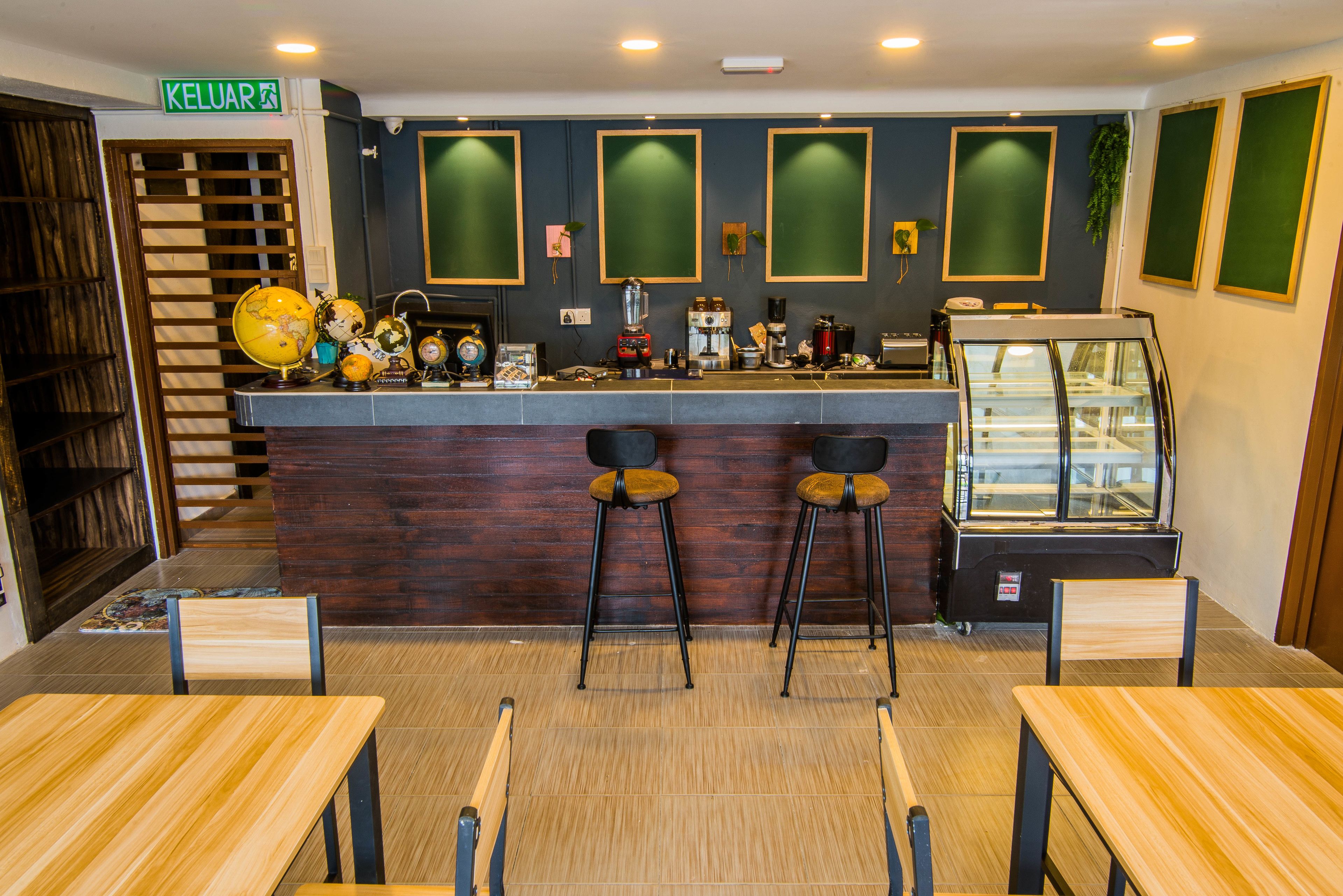 A restaurant interior with wooden tables and chairs, a counter with various appliances, and a display case.