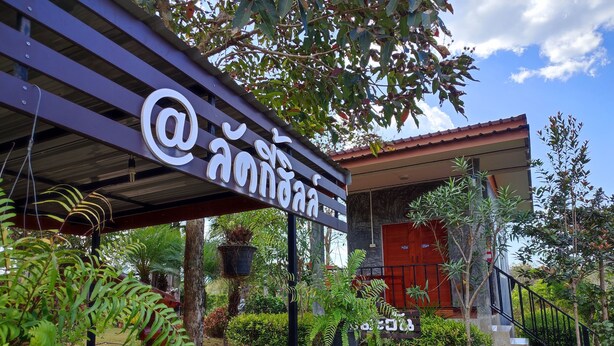 Entrada de hotel con un letrero, una escalera y un jardín con diversas plantas.