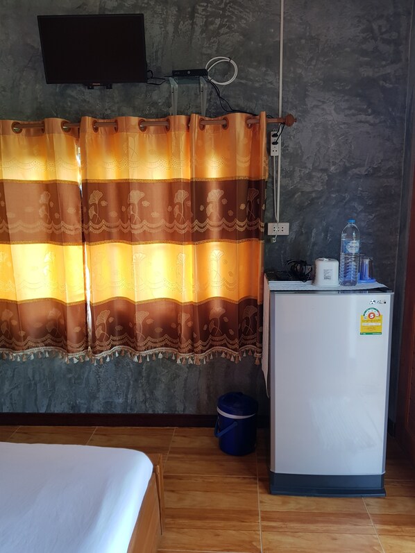 A room with a bed, a small refrigerator, a water dispenser, and a curtain with floral patterns.