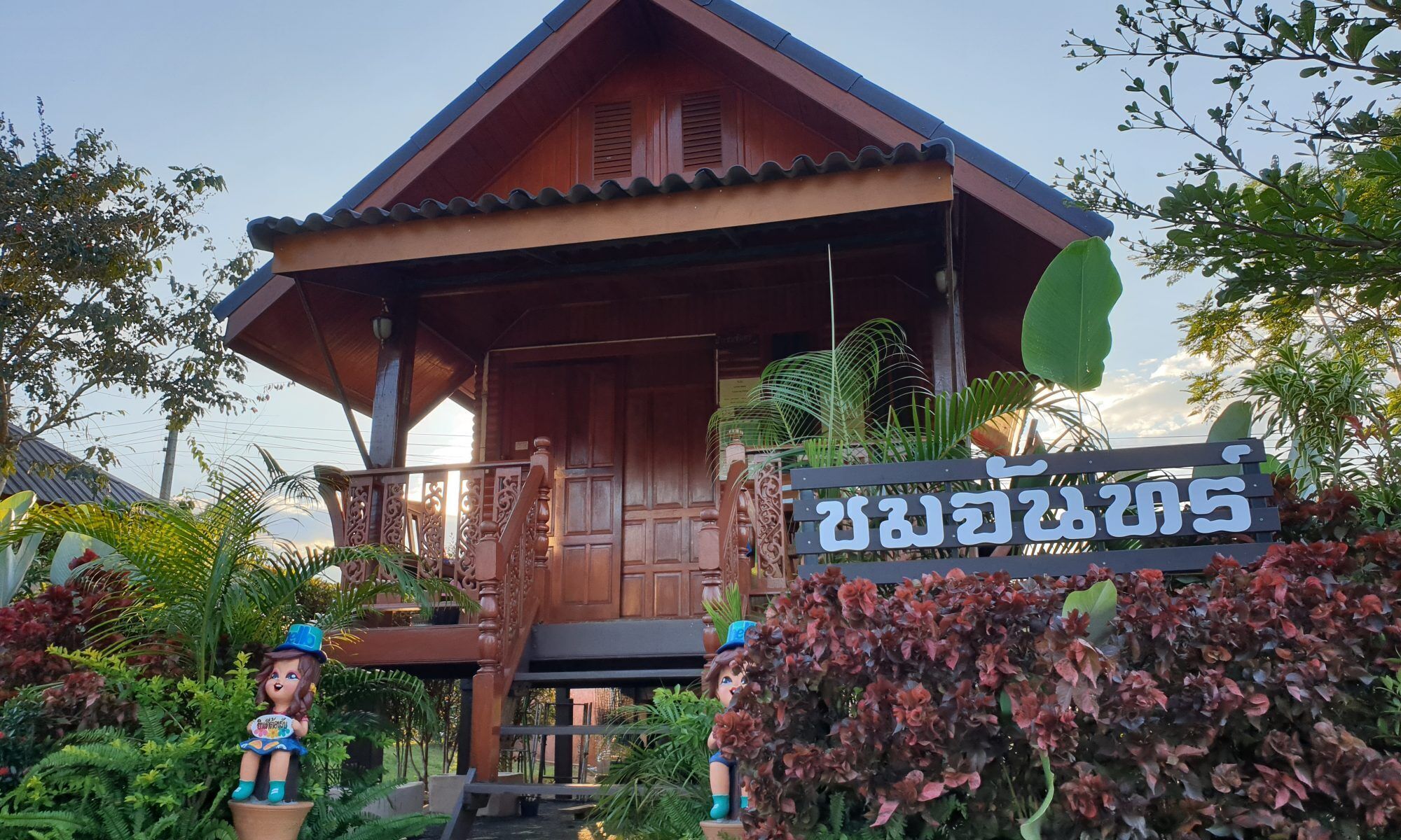 A wooden house with a porch, a sign with text, and decorative statues.