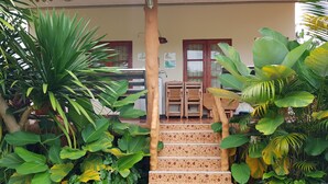 Una escalera conduce a un edificio con suelo de baldosas, rodeado de exuberante vegetación.