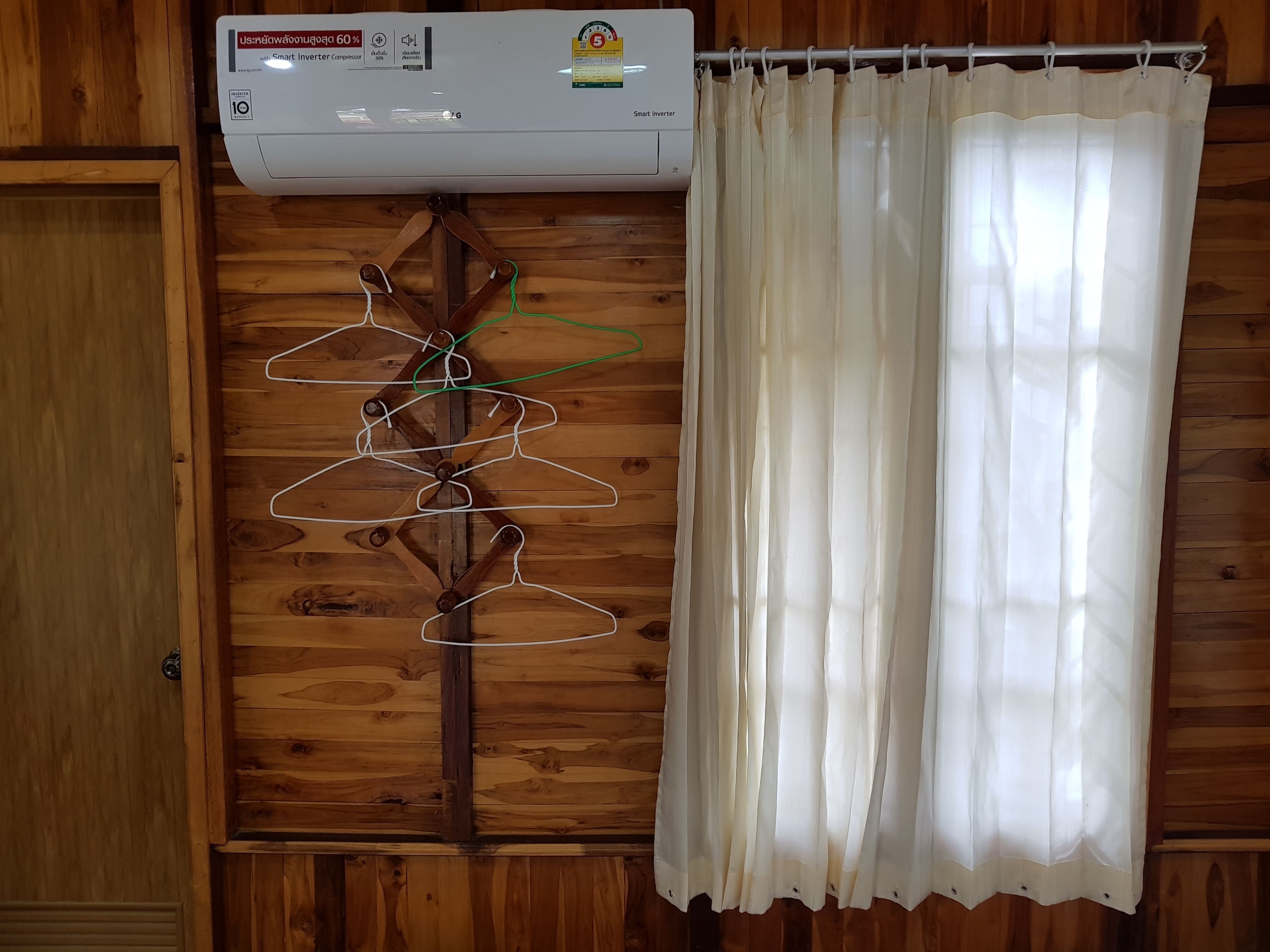 Een kamer met een houten wand, een witte airconditioning en een witte gordijn.