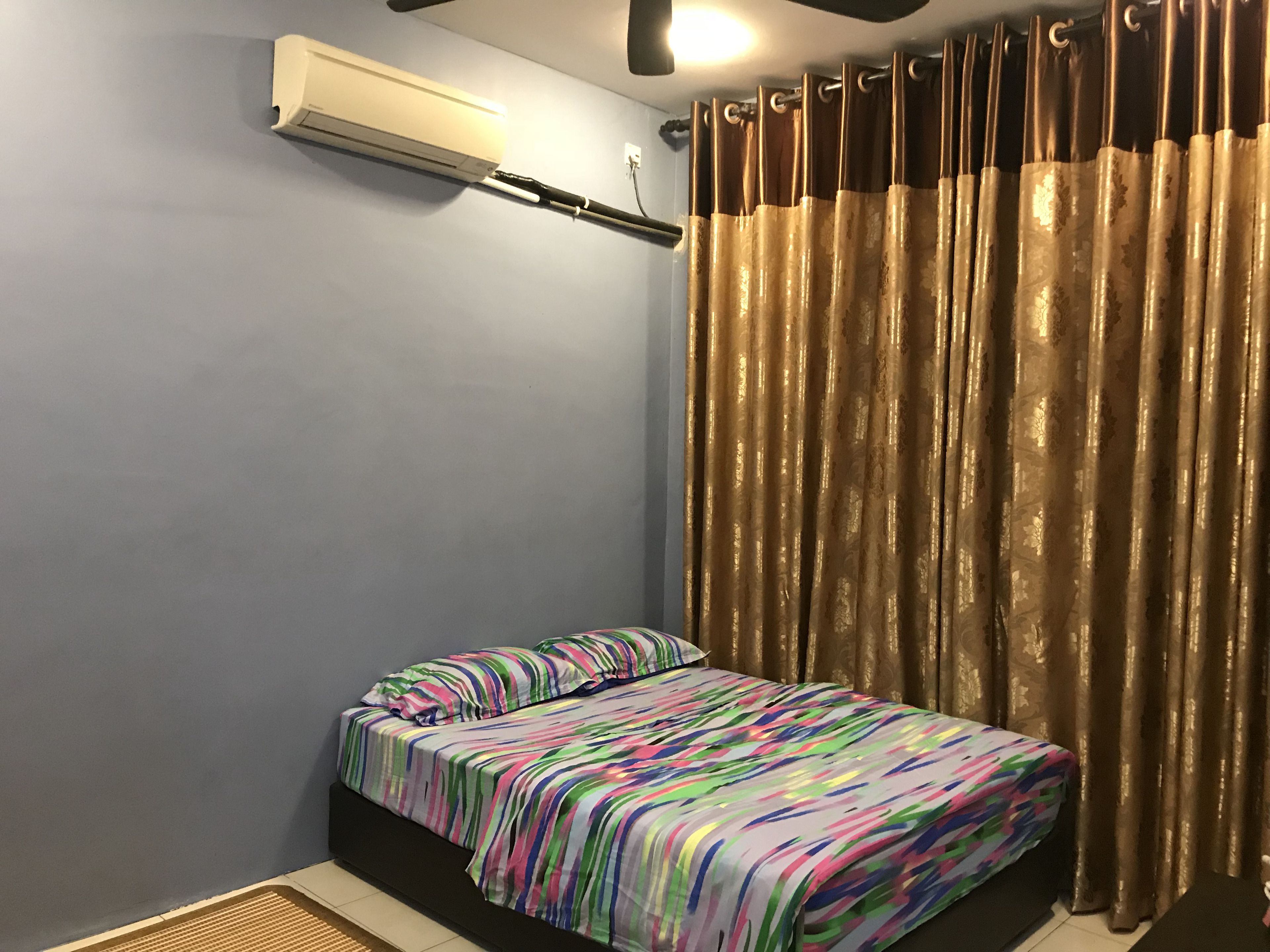A small bedroom with a bed, a window with curtains, an air conditioner, and a radiator.