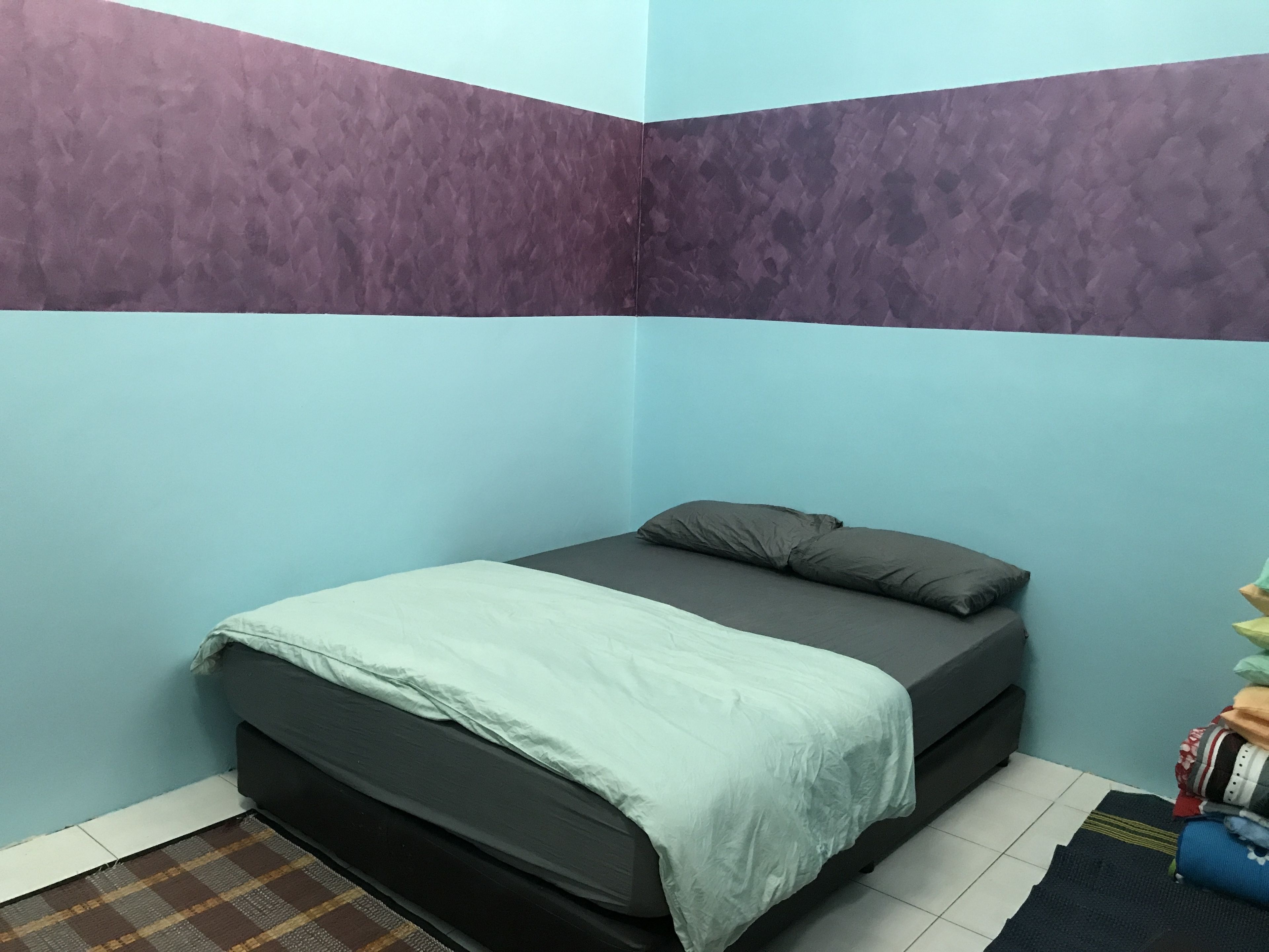 Un dormitorio con cama, almohadas, una alfombra y una pared con textura particular.