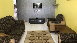 A living room with a flat-screen TV mounted on a textured gray wall, a black entertainment unit below, and patterned sofas. - Aushaf Homestay Changlun (Changlun)