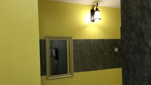 A bathroom with a mirror, a wall-mounted light fixture, and a textured wall panel. - Aushaf Homestay Changlun (Changlun)