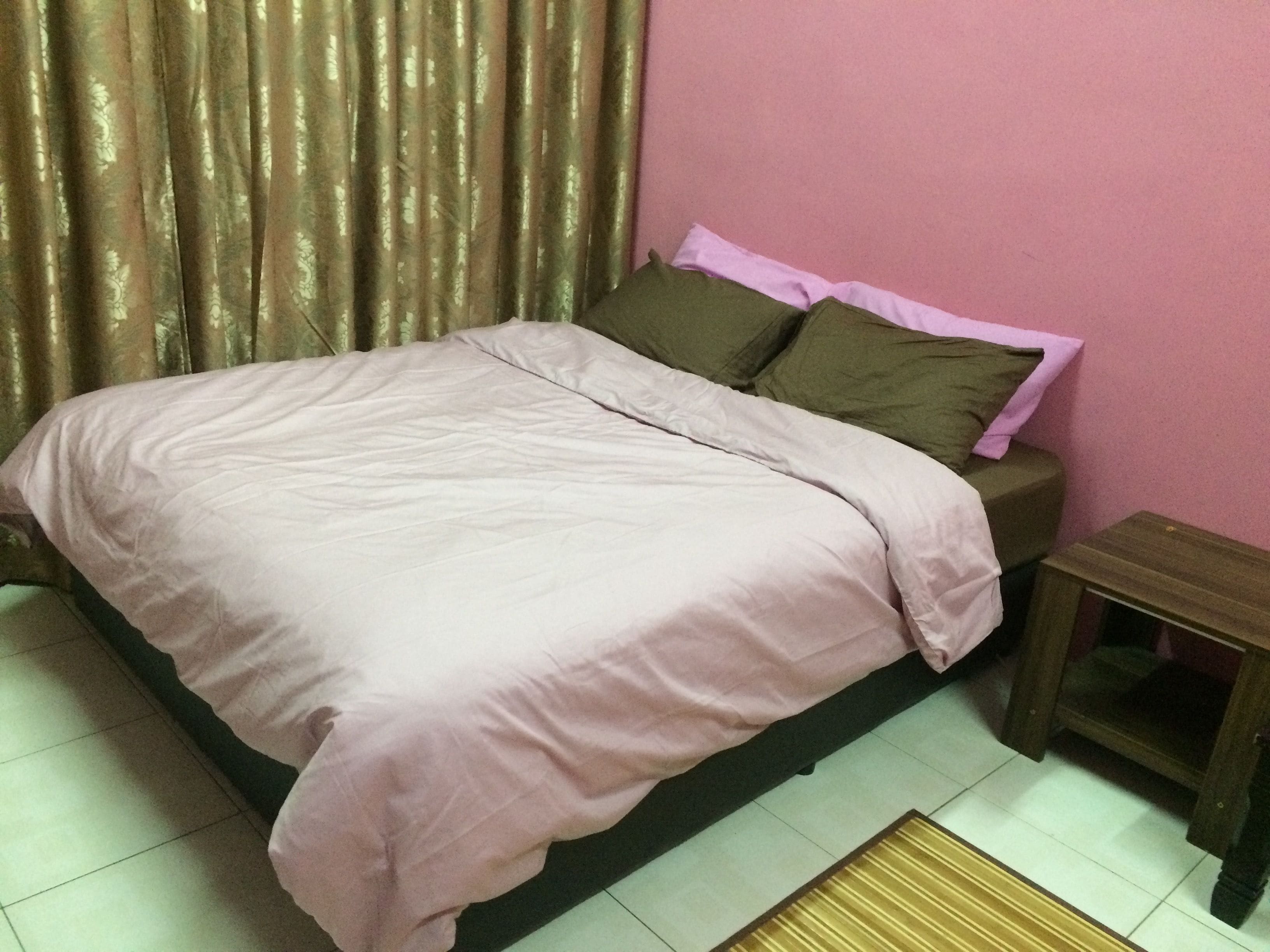 Una cama bien hecha con una colcha rosa y almohadas, una mesita de noche de madera y una pequeña mesa.