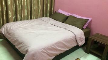 Una cama bien hecha con una colcha rosa y almohadas, una mesita de noche de madera y una pequeña mesa.