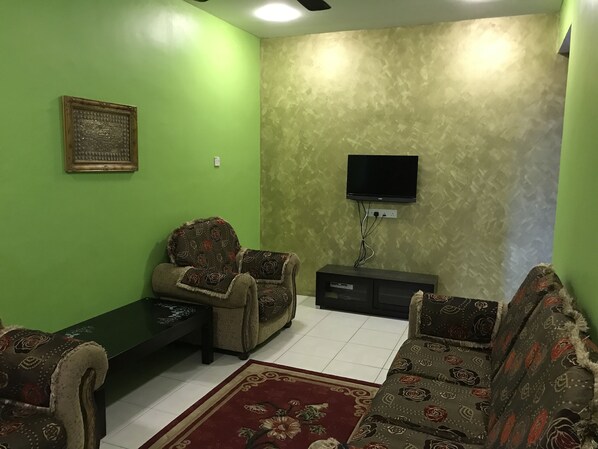 Una sala de estar con paredes verdes, un conjunto de sofá, una mesa de centro y un televisor de pantalla plana montado en la pared.