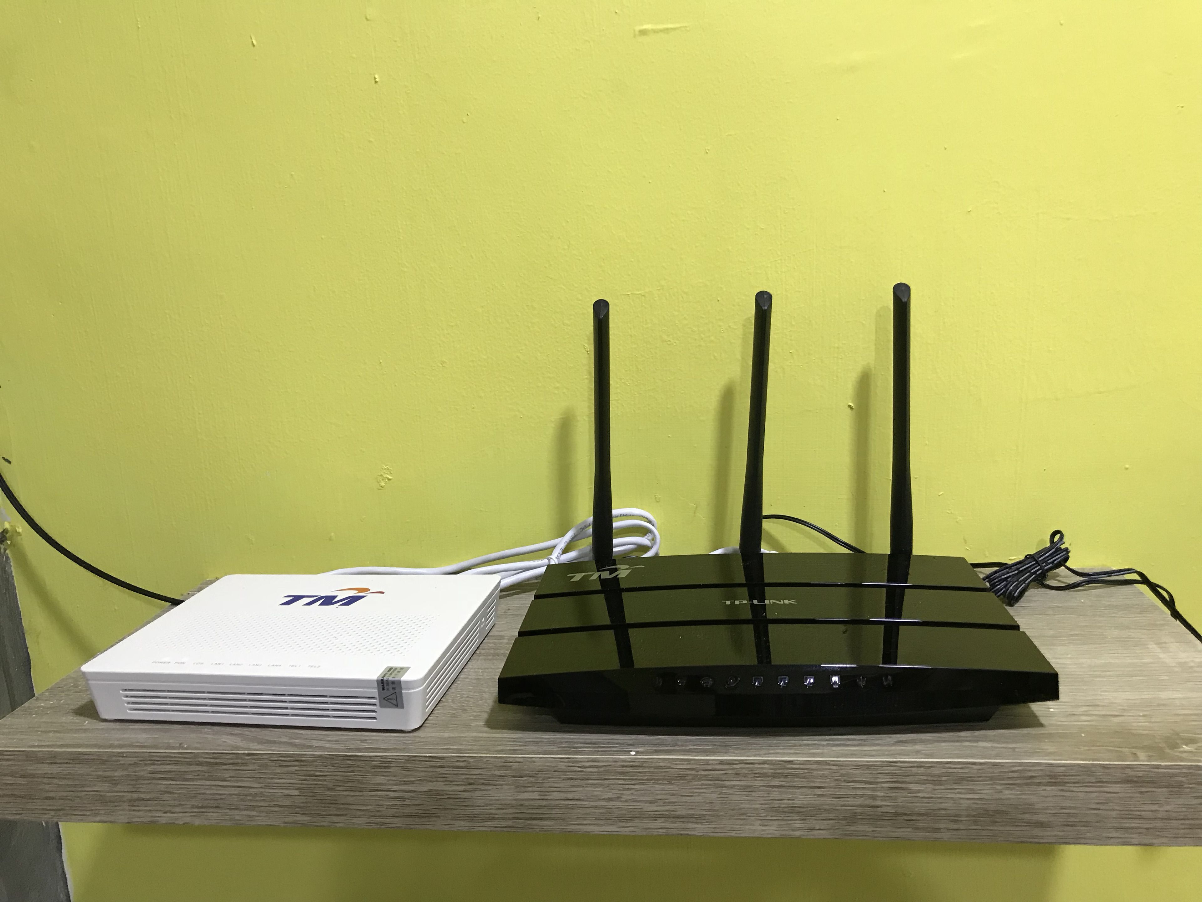 Un router con múltiples antenas sobre una superficie de madera, frente a una pared amarilla.
