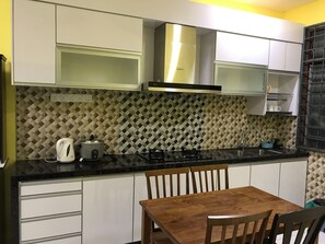 Una cocina con armarios blancos, encimera negra, estufa y mesa de comedor de madera con sillas.
