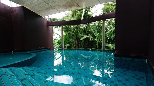 A swimming pool with tiled flooring and a view of lush greenery outside. - Hotel on Hilltop (Kathu)
